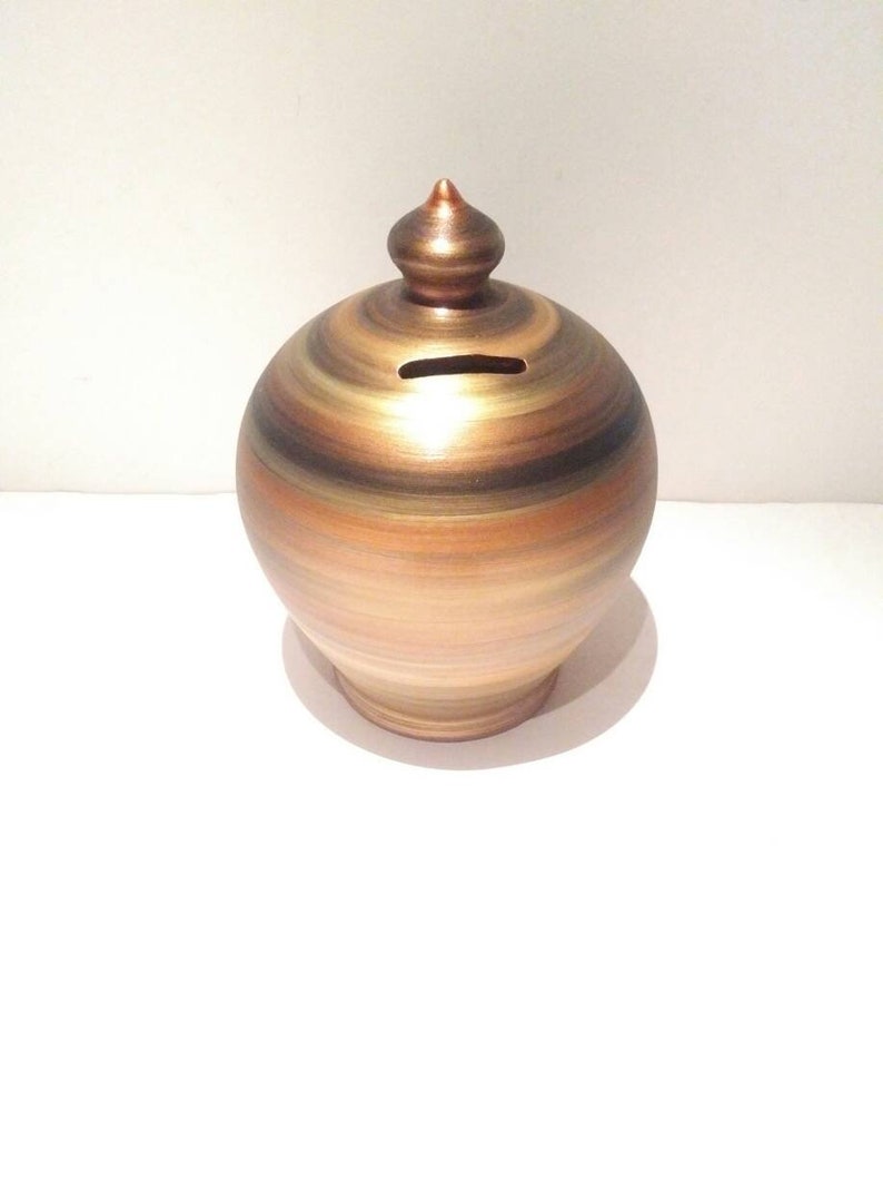 Infused with the luminus energy of the Sun, Gold, according to Feng Shui, attracts abundance, wealth, and prosperity. Our handmade and hand painted coin bank is an elegant addition to your home decor and an inspired gift for any feng shui enthusiast! Personalized Pottery Piggy Bank. Made to order.  Size: 20 cm = 7.874 Inches. Circumference: 52 cm = 20 inch. Colors: Metal Copper, Gold and Black, as in picture.  With hole and stopper plug, or without hole..